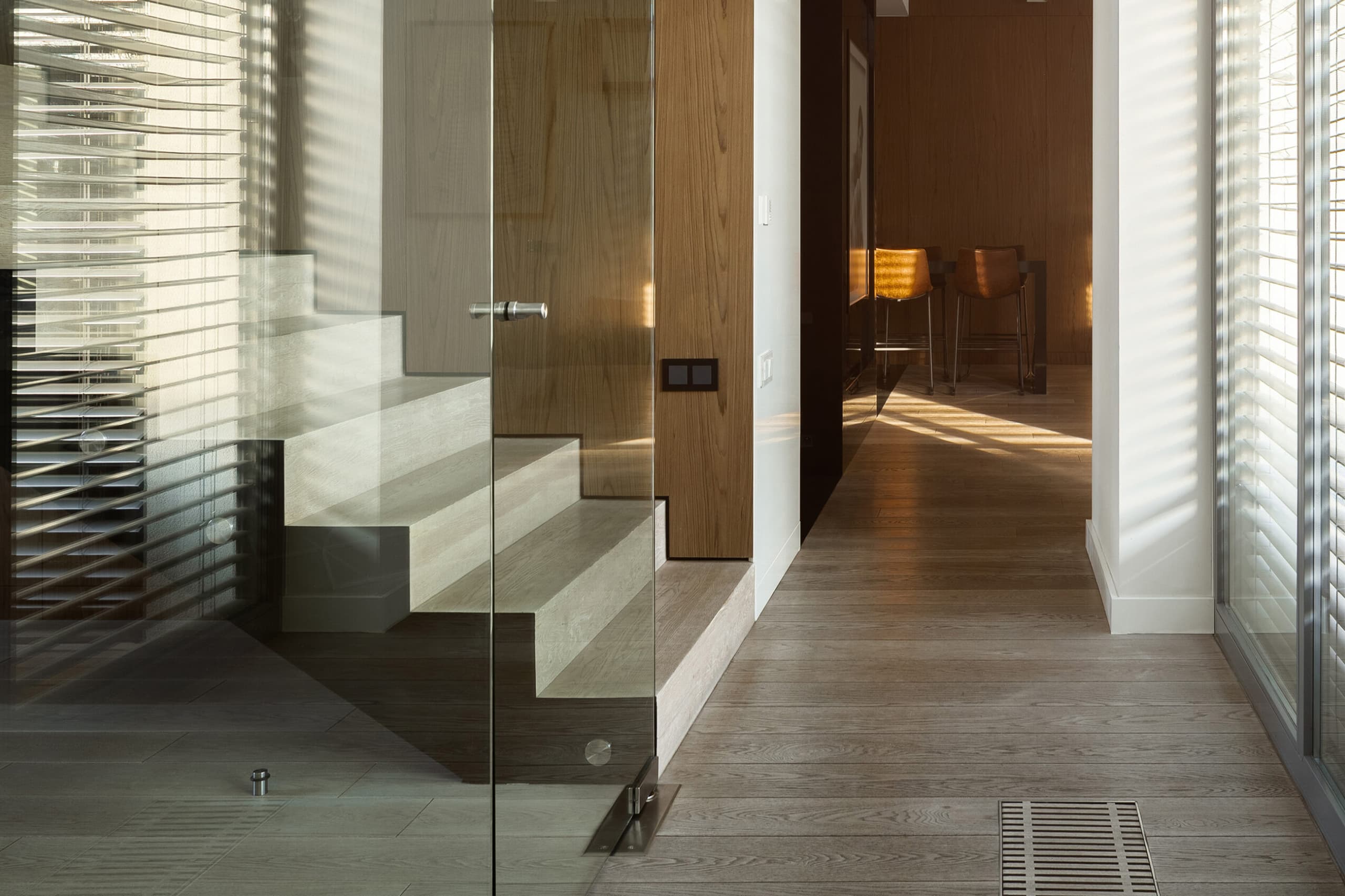 Wohnbereich mit Naturstein-Treppe und Holzboden, Glas-Geländer, warme Sonneneinstrahlung